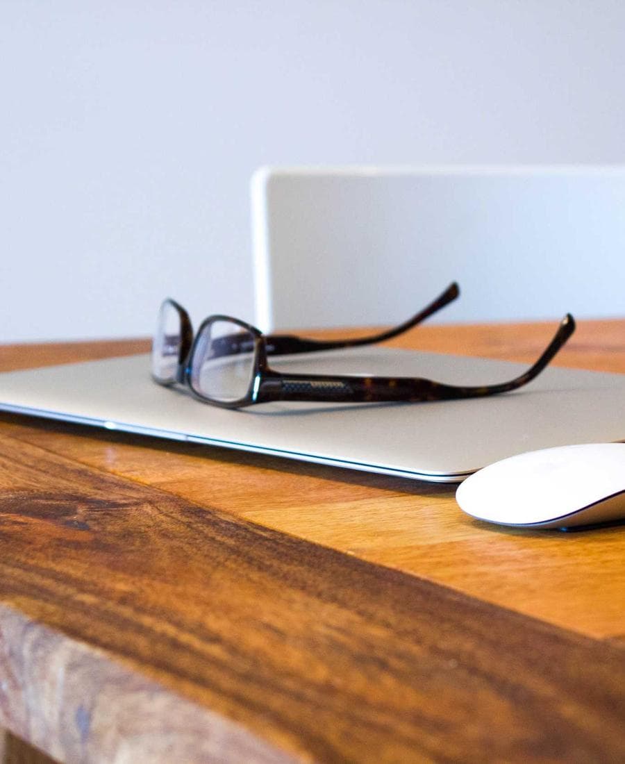 Laptop, glasses and mouse arranged on a wooden surface
